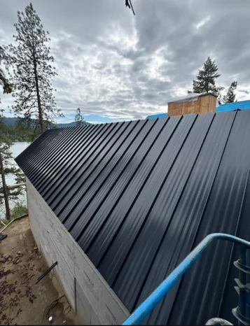 Completed black metal roof panels on a lakeside home by DG Contracting